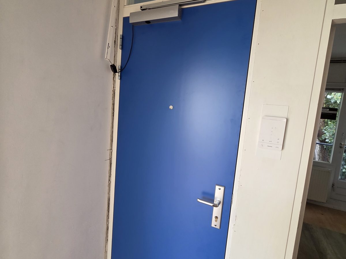 Blauwe voordeur met deurdranger in een portiek, afgehangen door Quickframe